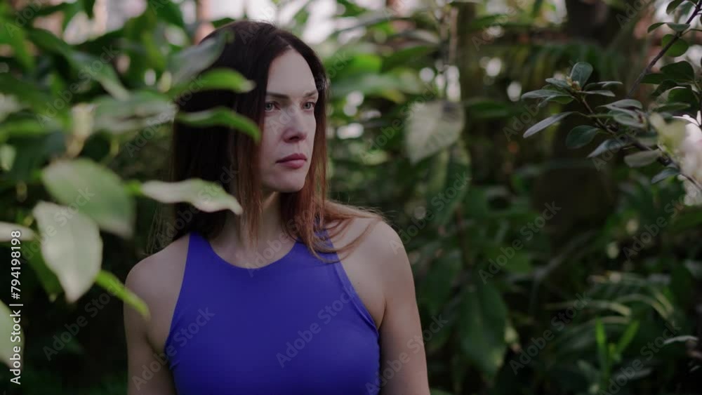 A woman in a tropical garden looking at plants and smelling flowers A woman in a tropical garden looking at plants and smelling flowers