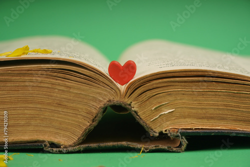 The photo shows an open book on the pages of which lies a plastic heart. This image can symbolize a love of reading or a combination of romantic and educational themes. An open book indicates access t