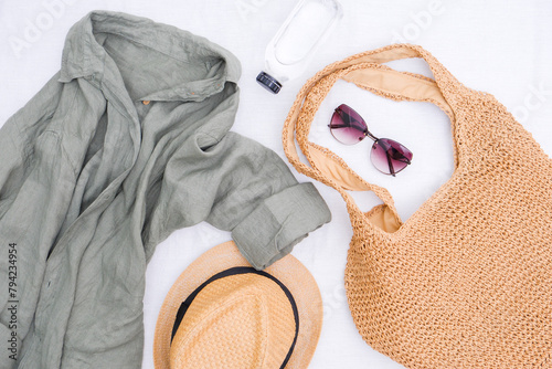  Look of women for spring summer. Linen shirt, Straw bag for beach, bottle of water, straw hat and sunglasses on white background. Summer and beach accessories.