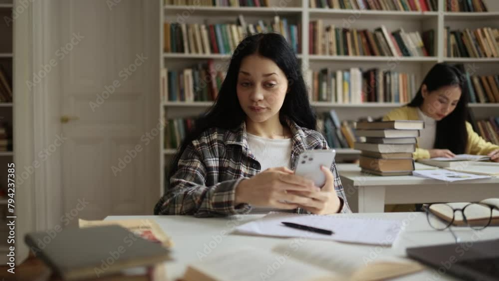 Portrait of charming young woman student looking at smartphone screen with nod of approval at university library and show at phone indoors Advise Approve Recommend Choice concept Portrait of charming young woman student looking at smartphone screen with nod of approval at university library and show at phone indoors Advise Approve Recommend Choice concept