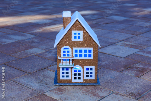 Beautiful toy two-story house with blue light in the windows on the background of paving slabs