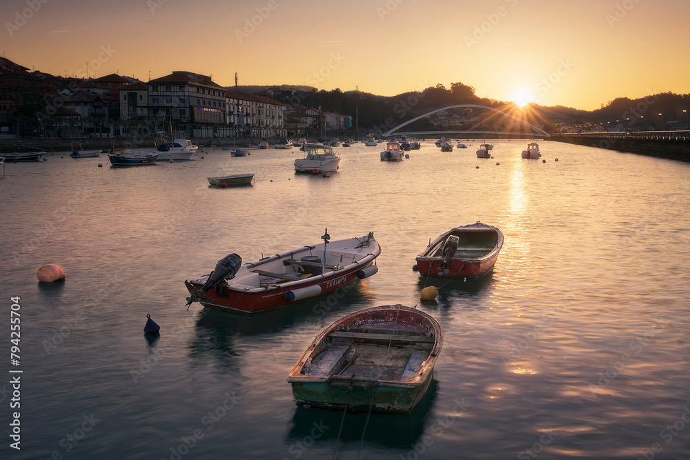 Boats at dawn in the Plentzia estuary with the sun rising behind the mountains leaving a warm atmosphere and an orange sky