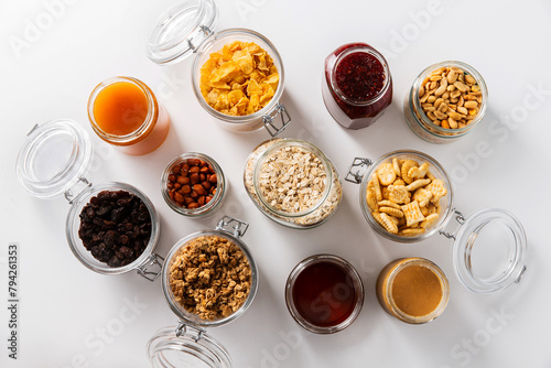 food storage and eating concept - close up of jars with oat, corn flakes, granola, cookies and spreads on white background photo