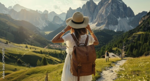   A woman in a white dress and hat gazes at mountains, holding a brown bag on her shoulder photo