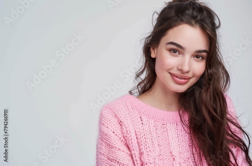  A woman, sporting long hair and wearing a pink sweater, beams at the camera against a pristine white backdrop