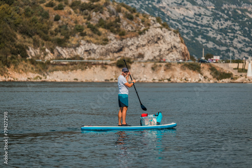 man enjoying stand-up paddleboarding on a calm sea with mountainous landscape in the background