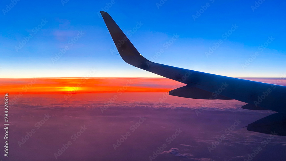 Fototapeta premium Sunset or sunrise from an airplane. Aerial view of a very colorful sky with the silhouette of an airplane wing in the foreground.