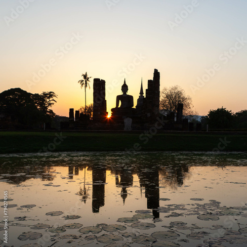 Old sitting Buddha statue and pagoda at sunset reflecting in the pond. Sukhothai Historical Park. Thailand. photo