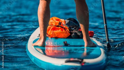 close-up of a man's legs paddleboarding in clear blue waters with safety gear on board photo