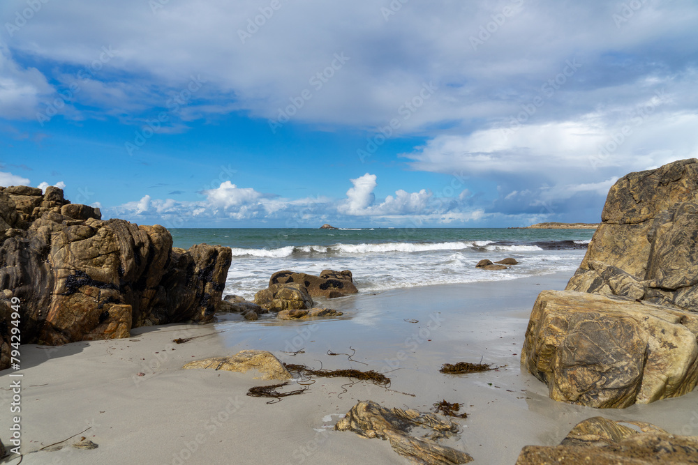 Sur le sable humide d'une plage bretonne, de beaux reflets des nuages aux couleurs contrastées se mêlent aux énormes rochers, créant un spectacle captivant.