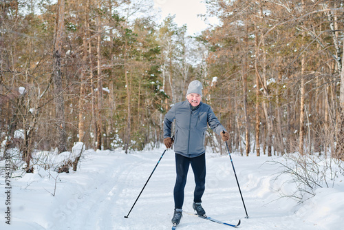 Wide shot of modern sporty senior Caucasian man skiing along forest road on winter day smiling at camera, copy space