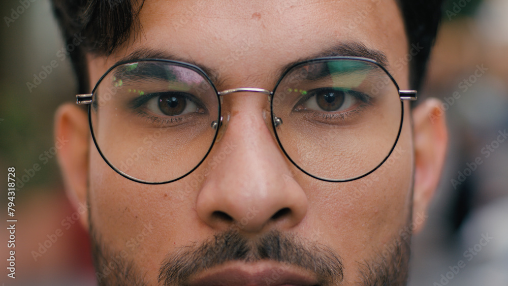 Close up calm confident relaxed Indian Arabian ethnic male student client man guy businessman model face glasses opening beautiful brown eyes iris looking at camera outdoors city street. Ophthalmology