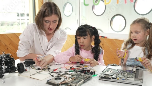 Skilled caucasian teacher teach and explain students about digital electrical tool. Expert girl learn electronic equipment and use to fix motherboard at table with chips and wires placed. Erudition. photo