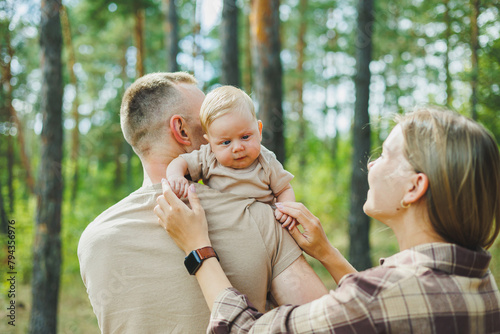 A walk of dad and mom with a baby in the park. A happy family couple with a small newborn baby in their arms are standing in nature. Family vacation with a small child