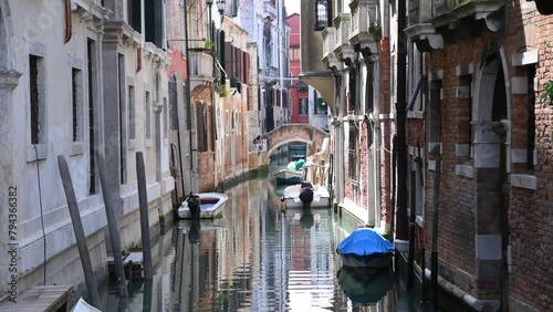 Venetian old narrow canals with buildings on both sides and boats parked on water.