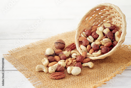 Nuts Mix in a Wooden Plate on a White Background. Wicker Basket full of Cashew, Walnuts, Hazeltuts, Peanuts, Brazilian Nuts, Pistachios on a Burlap with Side View