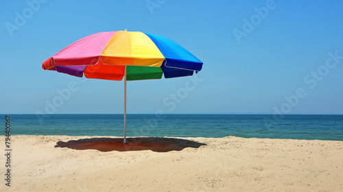Colorful beach umbrella stands alone on a tranquil sandy beach with clear blue skies photo