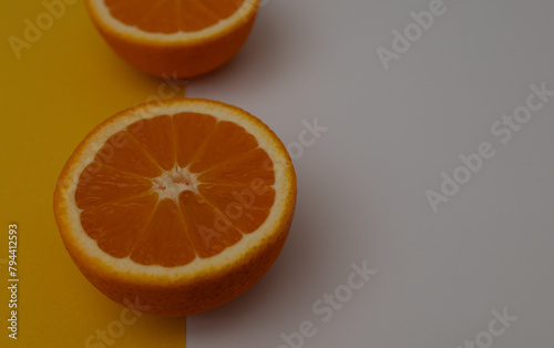 oranges are cut in half and placed on a yellow and white background. The oranges are ripe and juicy  and their bright orange color contrasts with the neutral background