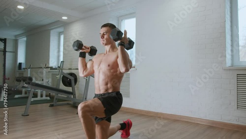 Young muscular man is training in gym and doing exercises with dumbbells. Achieving success and improving results with regular training photo