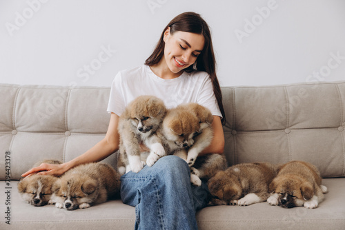 Portrait of happy smiling millennial woman hugging and playing group Akita Inu puppies on sofa at home
