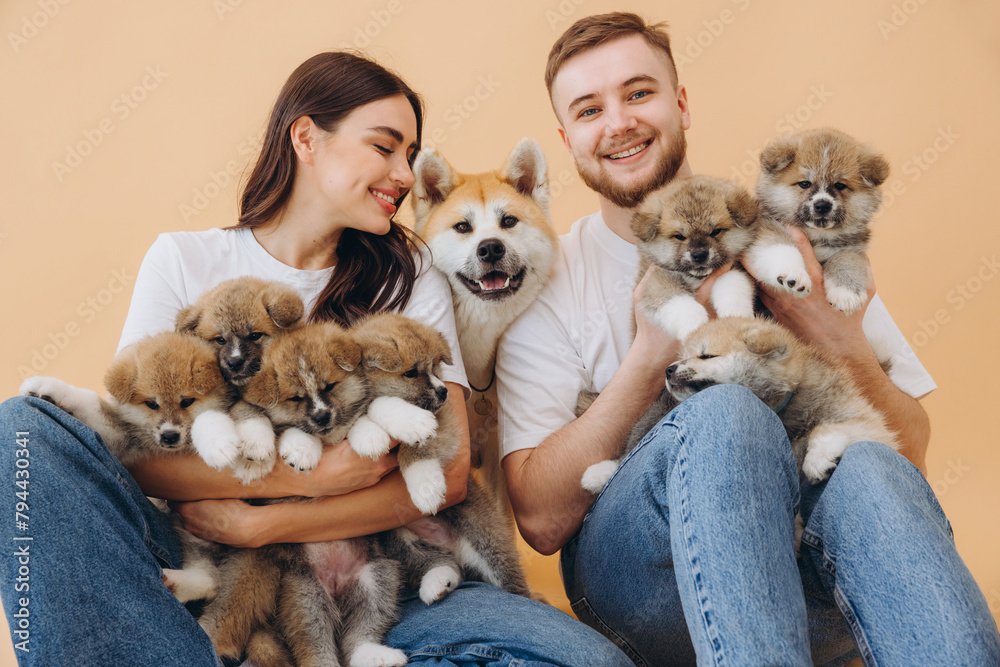 Happy beautiful couple in love caring and playing with little funny puppies and their mother dog on beige background, banner, world animal day, concept: breeding and selling puppies Akita-Inu