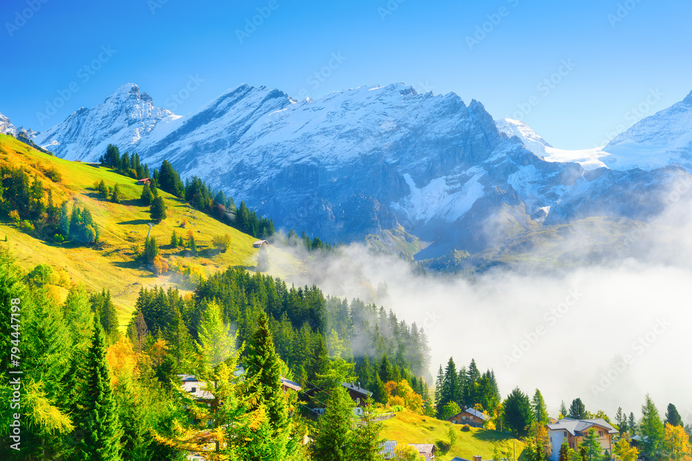 Village in Switzerland. A sunny day and a mountain valley. Houses on the mountains background. Meadow and forest in mountains. Classic Swiss view.