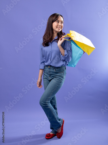 Joyful shopper with colorful bags  blue blouse  denim jeans  and red flats on a purple backdrop