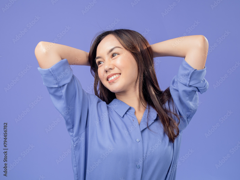 Portrait of an Indonesian Asian woman, wearing a blue shirt, smiling with her hands behind her head, isolated against a purple background Portrait of an Indonesian Asian woman, wearing a blue shirt, smiling with her hands behind her head, isolated against a purple background