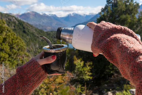 Hands holding a mate with Argentine yerba, with mountains and lakes in the background. Patagonia, Argentina.