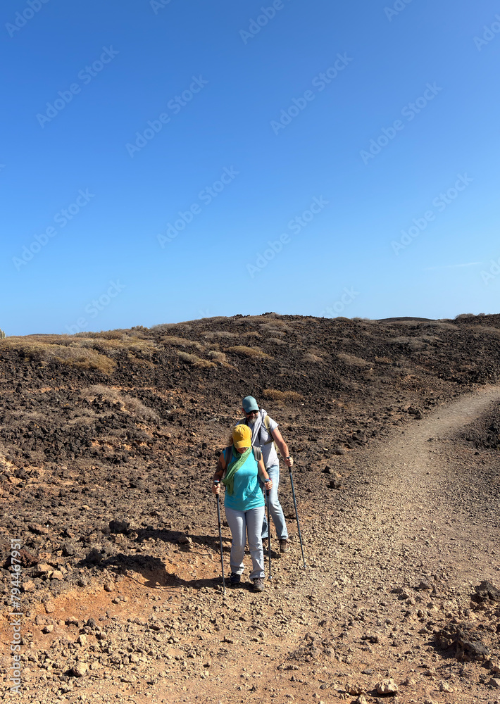 Outdoor activity in nature concept. Active middle aged couple hiking together in arid footpath enjoying healthy lifestyle and freedom. Blue sky in sunny good day
