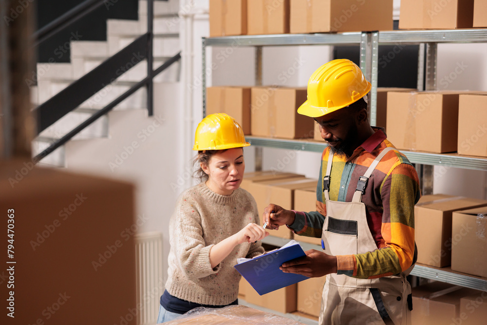 Diverse stockroom looking at products logistics report, while preparing clients orders in warehouse. African american supervisor working at products inventory with worker in storage room Diverse stockroom looking at products logistics report, while preparing clients orders in warehouse. African american supervisor working at products inventory with worker in storage room