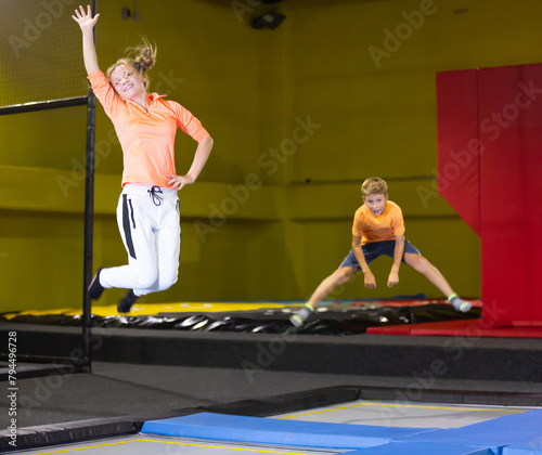 Excited teen girl in orange sports jumper and white pants jumping and indulge on trampolines in entertainment center