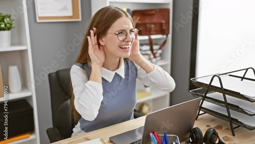 Curious young blonde business woman trying to hear office gossip, hand on ear in a gesture of deaf problem. bound to silence, her expression screams the unsaid. photo