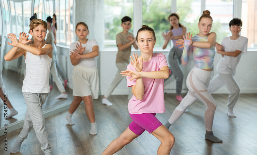 Group of teenagers performs modern dances during class at choreographic school. Additional extracurricular activities for children and teenagers. Female teacher in background dances with students