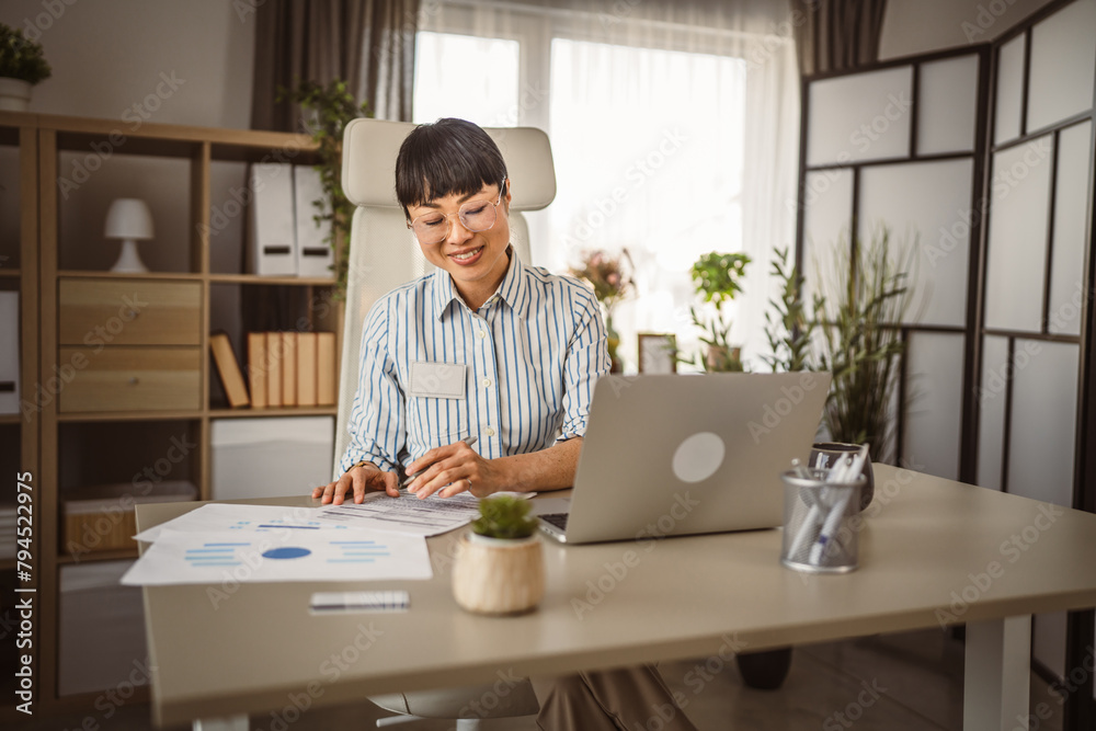 Mature japanese woman with eyeglasses sit and sign document at the office Mature japanese woman with eyeglasses sit and sign document at the office
