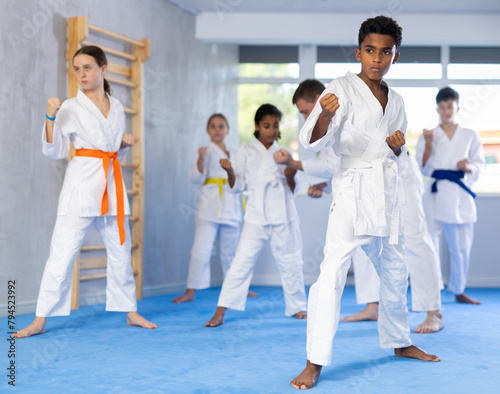 Group of boys and girls in kimonos train karate techniques in studio..