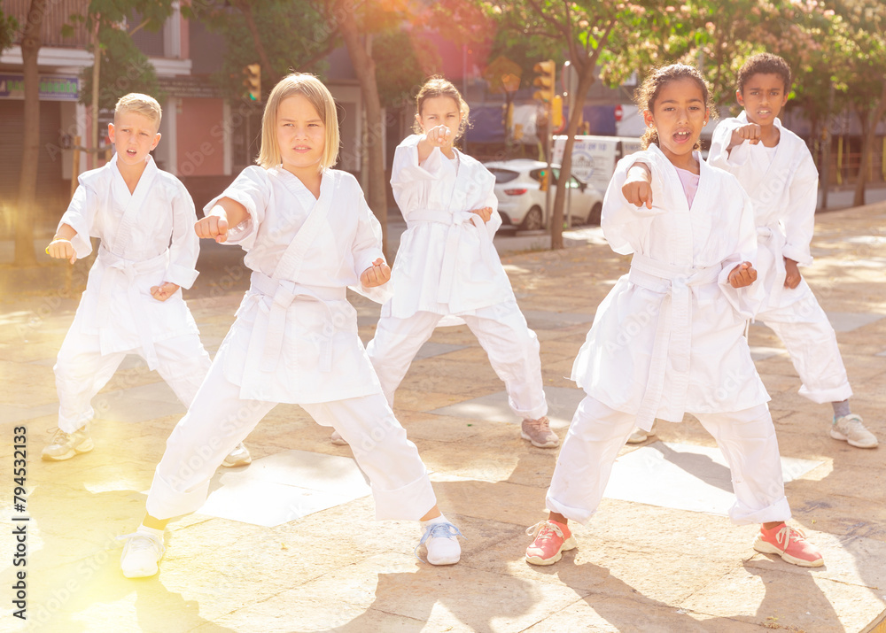 Multiracial group of concentrated preteen children practicing karate movements during outdoors group class on summer city street