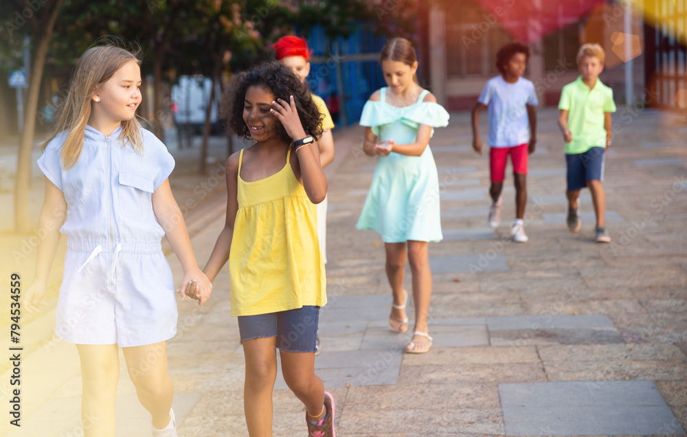 Two cheerful cute preteen girls enjoying walk along city street on summer day..