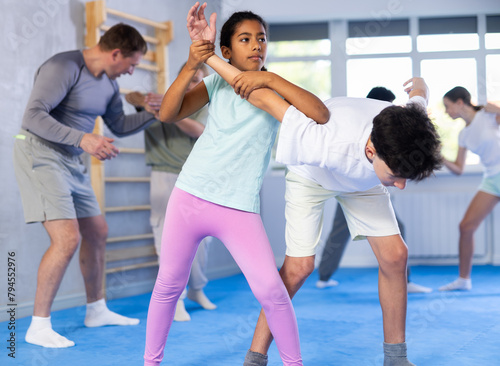 Determined black tween girl practicing armlock, painful control move to hold and immobilize opponent, in training bout with boy during self defence course in gym ..