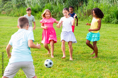 Group of barefoot kids playing football on grass. They're kicking ball and having fun.