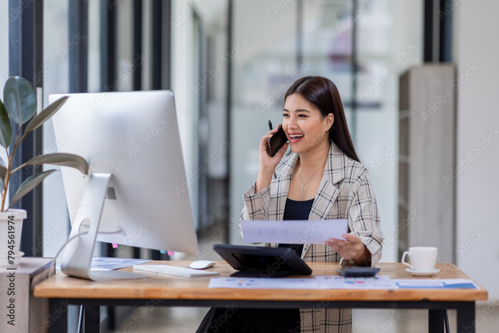 Obraz premium Asian woman entrepreneur busy with her work in the office. Young Asian woman talking over phone or cellphone while sitting at her desk. 