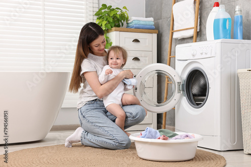 Mother with her daughter washing baby clothes in bathroom