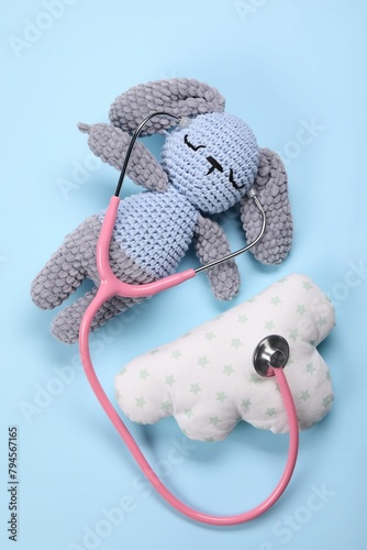 Toy bunny, pillow and stethoscope on light blue background, flat lay