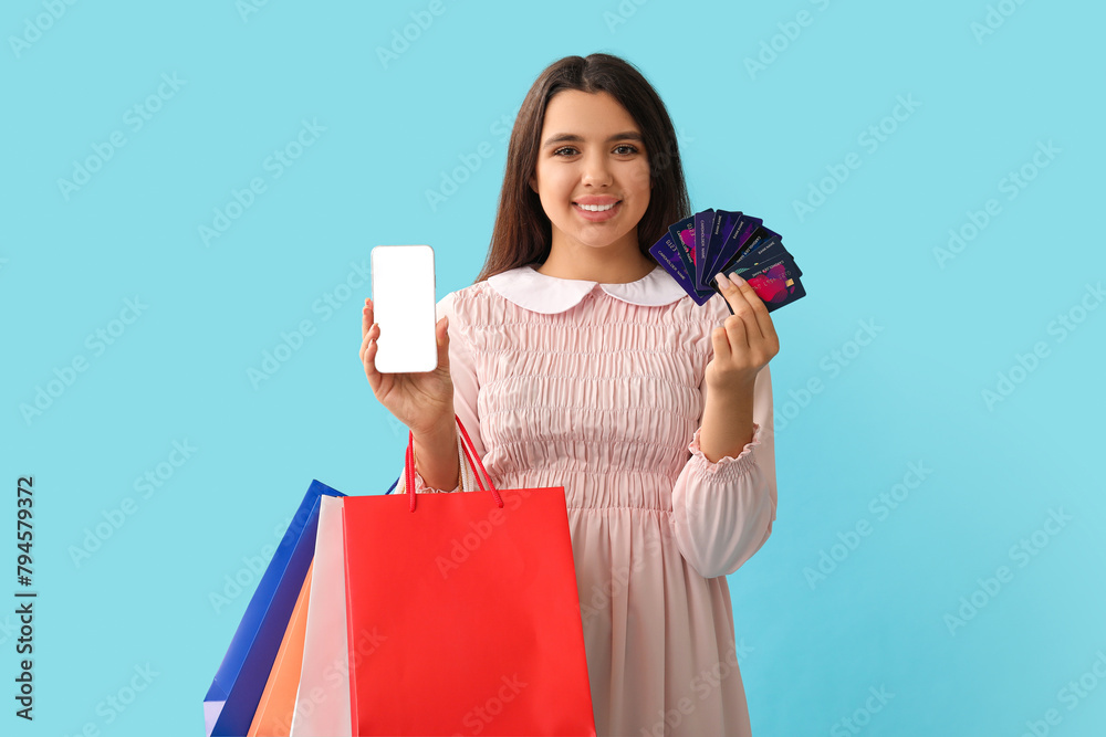 Young woman with credit cards, mobile phone and shopping bags on blue background Young woman with credit cards, mobile phone and shopping bags on blue background