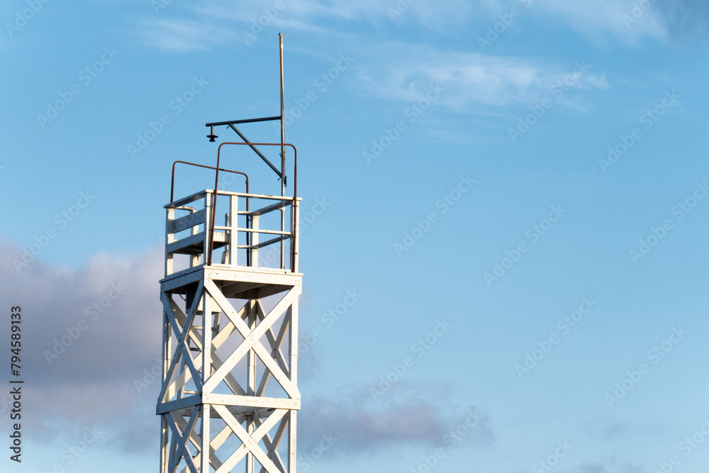 A white wooden lookout climbing tower on a blue sky A white wooden lookout climbing tower on a blue sky