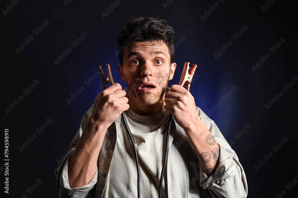 Electrocuted young man with burnt face and jumper cables on dark background Electrocuted young man with burnt face and jumper cables on dark background