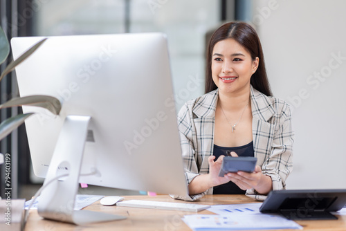Young happy professional business asian woman employee sitting at desk working on laptop in modern corporate office interior. Smiling female worker using computer technology typing browsing web.