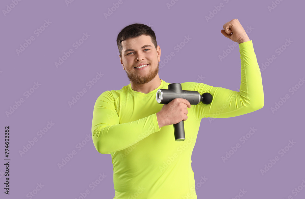 Sporty young man massaging his arm with percussive massager on lilac background Sporty young man massaging his arm with percussive massager on lilac background