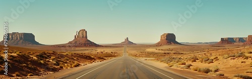 A long road leading to the desert with rock formations in it, with a blue sky. The mountainous land of wash and monument valley photo