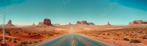 A long road leading to the desert with rock formations in it, with a blue sky. The mountainous land of wash and monument valley